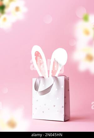 Orecchie coniglietto di Pasqua in un sacchetto di carta. Sfondo rosa. Spazio per il testo. Buona pasqua Foto Stock