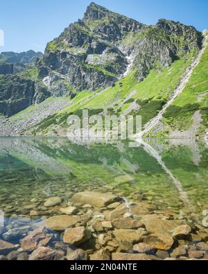 Prominente montagna rocciosa che si riflette in un lago alpino cristallino, tiro verticale, Polonia, UE Foto Stock