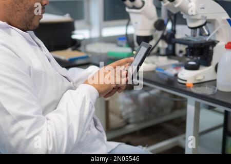 Ricercatore anonimo utilizzando un tablet in un laboratorio moderno. Primo piano delle mani che scrivono sul tablet Foto Stock