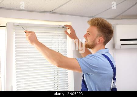 Handyman con cacciavite che installa le tende della finestra all'interno Foto Stock