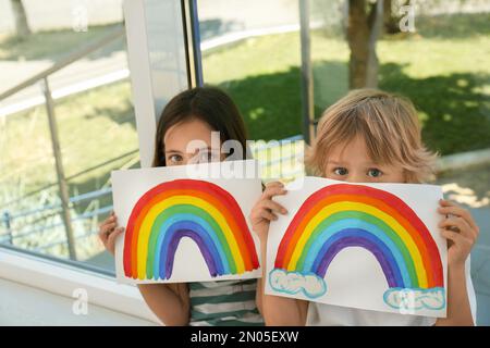 Bambini piccoli che tengono dipinti arcobaleno vicino alla finestra al coperto. Concetto di soggiorno a casa Foto Stock