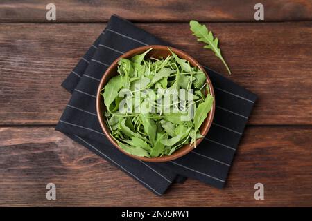 Foglie di rucola fresche in ciotola su tavola di legno, piatto Foto Stock