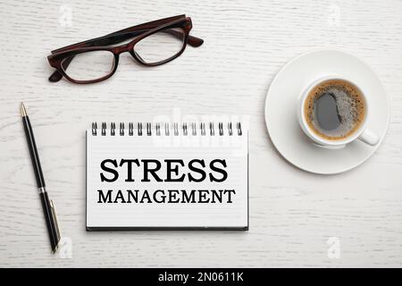 Testo stress Management in notebook su tavolo con occhiali, penna e tazza di caffè su tavolo di legno bianco, piatto Foto Stock