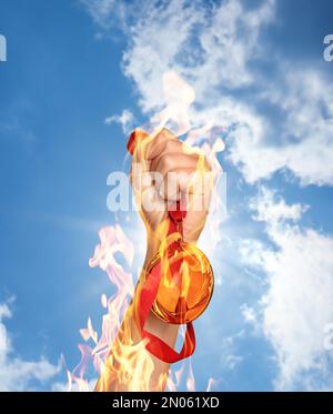 Vincitore che alza la mano con la medaglia d'oro dalle fiamme fino al cielo, primo piano Foto Stock