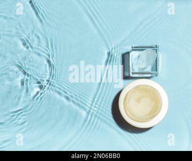Swatch di crema su podio di vetro con vaso su fondo acqua. Concetto di cosmetici idratanti Foto Stock