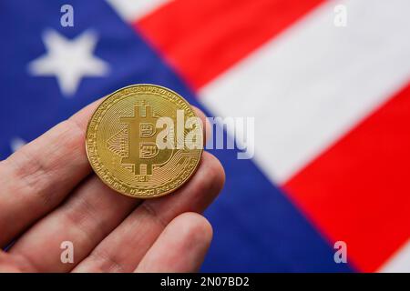 Mano con bitcoin dorato BTC e bandiera USA sullo sfondo. Crypto investe negli Stati Uniti d'America. Foto Stock