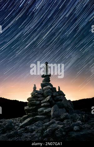Cielo notturno con sentieri stellari su arrangiamento in pietra bilanciata impilato, composizione verticale centrata Foto Stock
