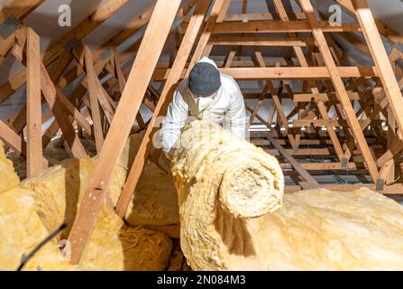 l'uomo isola il tetto e il soffitto della casa con lana di vetro Foto Stock