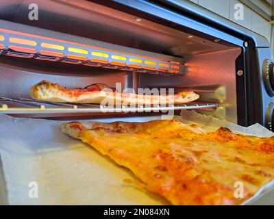 Fetta di formaggio pizza primo piano vita reale in cucina, riscaldare nel forno elettrico Foto Stock