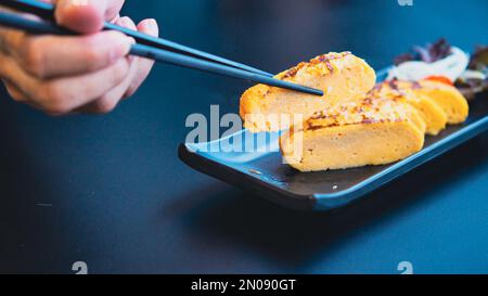 choppstick Hold Tamagoyaki, omelette dolce Soft Focus in giapponese Foto Stock