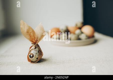 Quaglia e uova di pollo. Sfondo tessile grigio. Buona Pasqua. Decorazione di orecchie coniglietto di Pasqua. Foto Stock