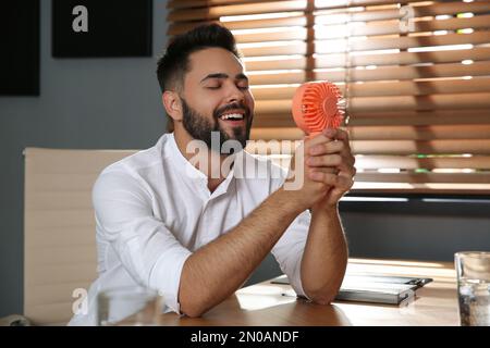 Uomo che gode del flusso d'aria dal ventilatore portatile sul posto di lavoro. Caldo estivo Foto Stock