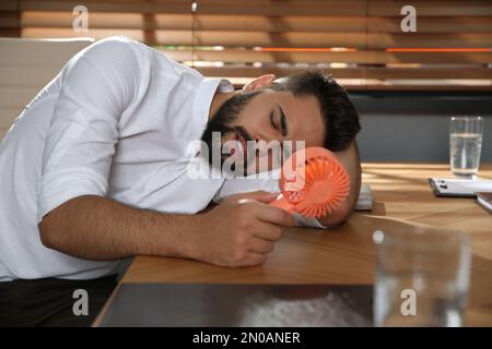 Uomo con ventola portatile che soffre di calore sul luogo di lavoro. Stagione estiva Foto Stock