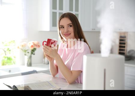 Donna che beve caffè in cucina con moderno umidificatore d'aria Foto Stock