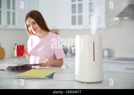 Moderno umidificatore d'aria e donna sfocata bere caffè in cucina Foto Stock