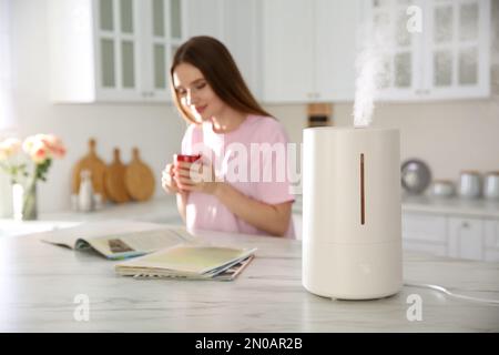 Moderno umidificatore d'aria e donna sfocata bere caffè in cucina Foto Stock