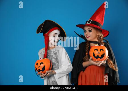 Carino bambini piccoli con secchi caramelle zucca indossare costumi di Halloween su sfondo blu Foto Stock