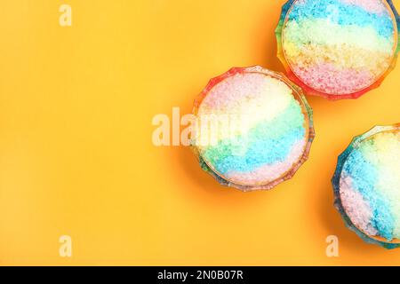 Rasatore di ghiaccio arcobaleno in ciotole di vetro da dessert su fondo arancione, piatto. Spazio per il testo Foto Stock