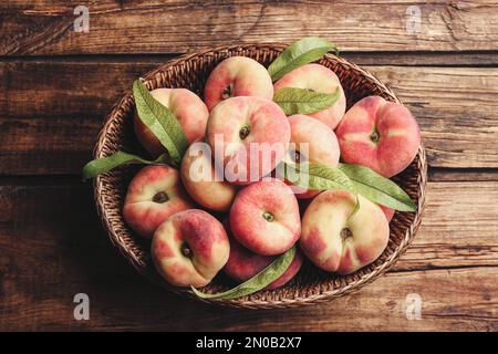 Pesche di ciambella fresche mature in cesto su tavolo di legno, vista dall'alto Foto Stock