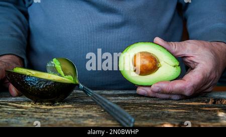 Uomo che tiene avocado in rustico tavolo di legno con spazio copia Foto Stock