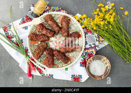 rotoli di carne tradizionali, detti “mititei” su un piatto di ceramica, con un bouquet di fiori di tazzina Foto Stock