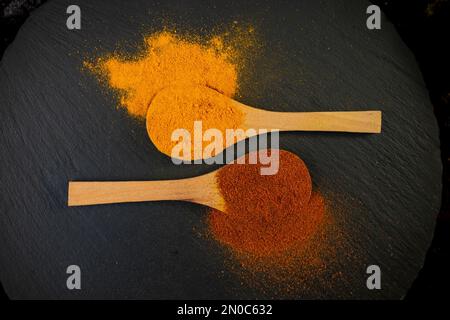 Due cucchiai da tè in legno con paprika affumicata e curcuma, su una lastra di pietra nera Foto Stock