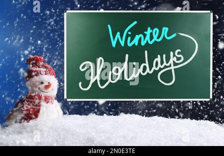 Texte sur Winter Holidays on School Chalkboard contro il pupazzo di neve decorativo in snowdrift Foto Stock