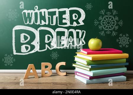 Testo Winter Break sulla lavagna della scuola vicino al tavolo con libri, lettere e mela Foto Stock