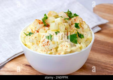 Insalata di patate Amish fresche fatte in casa con patate, uova sode, condimento cremoso e sedano in un recipiente bianco su un dorso di legno Foto Stock