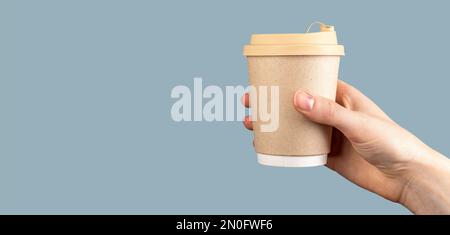 Mano femminile che tiene una tazza di carta di caffè su sfondo blu pastello, banner, spazio di copia. Tazza monouso da asporto di latte con coperchio. Ciao Foto Stock