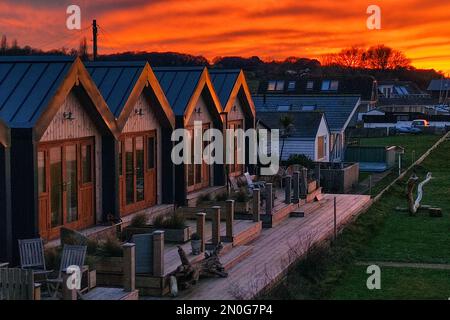 Una fila di case simili piccole e piccole vacanze sulla spiaggia sulla costa drammatico tramonto che riflette la linea del tetto apice dell'edificio Isola di Wight Foto Stock