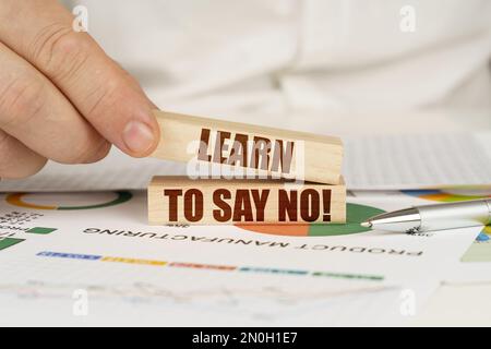 Concetto aziendale. Sulla tabella sono le tabelle di affari e i diagrammi nelle mani di un blocco di legno con l'iscrizione - Impara a dire No Foto Stock