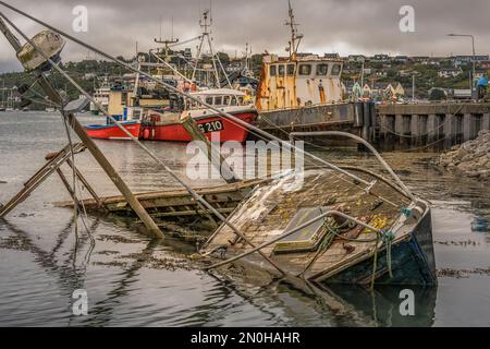 Vecchio, a metà affondato, una barca da pesca di fronte ad altre barche da lavoro, e navi nell'estuario del fiume Owenabue con Crosshaven villaggio sullo sfondo. Irlanda Foto Stock