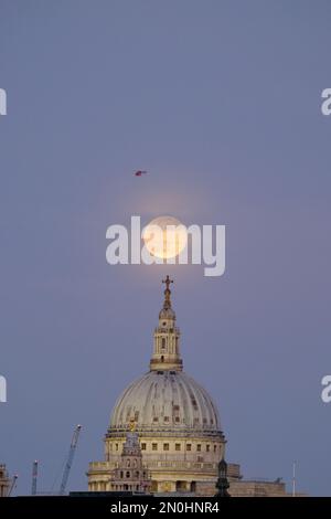 Londra, Regno Unito. 5th febbraio, 2023. Un'ambulanza aerea è vista di passaggio mentre la Luna piena di neve sorge da dietro la Cattedrale di San Paolo. Questo mese vede la luna più piccola dell'anno - conosciuta come una 'microluna', che appaiono 14% più piccola di una superluna. Credit: Undicesima ora di Fotografia/Alamy Live News Foto Stock