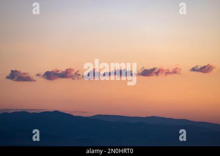 Un tramonto viola mozzafiato irradia la sua calda tonalità sulle maestose montagne, dipingendo il cielo con nuvole soffici. Foto Stock