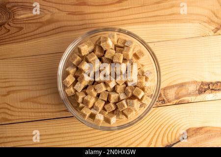 Diversi cubetti di zucchero di canna in una ciotola di vetro, primo piano, su un tavolo di legno, vista dall'alto. Foto Stock