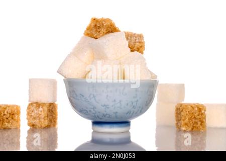 Diversi cubetti di zucchero di canna e zucchero bianco in una ciotola di ceramica, primo piano, isolati su bianco. Foto Stock