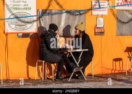 Donne che bevono caffè fuori dalla tenda arancione in una soleggiata giornata invernale a Kauppatori o in Piazza del mercato a Helsinki, Finlandia Foto Stock