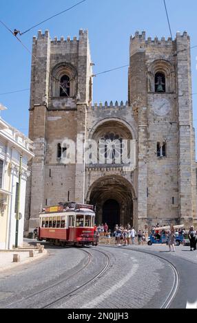 Facciata principale della cattedrale di Lisbona, con il tram numero 28 che passa attraverso la porta e i turisti che vedono il quartiere alfama, verticale Foto Stock