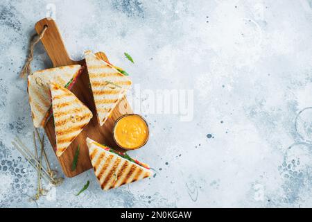 Quattro panini fatti in casa con salsiccia, formaggio e rucola su un fondo di cemento chiaro. Il concetto di un pasto veloce o uno spuntino al lavoro o a scuola. Foto Stock