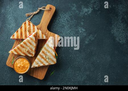 Quattro panini fatti in casa con salsiccia, formaggio e rucola su fondo di cemento scuro. Il concetto di un pasto veloce o uno spuntino al lavoro o a scuola. Parte superiore v Foto Stock
