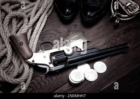 Old West revolver con gli Stati Uniti Badge Marshal e dollari d'argento con cappello, corda e stivali da cowboy Foto Stock