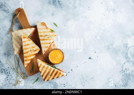 Quattro panini fatti in casa con salsiccia, formaggio e rucola su un fondo di cemento chiaro. Il concetto di un pasto veloce o uno spuntino al lavoro o a scuola. Foto Stock