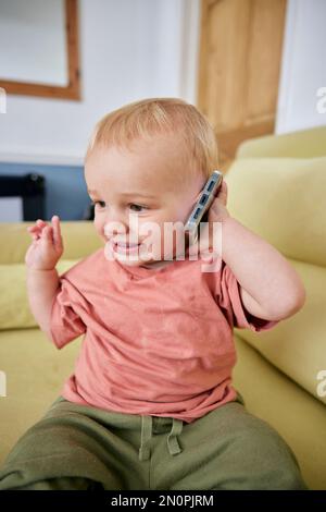 Bambino che tiene in mano uno smartphone con espressione animata in interni Foto Stock