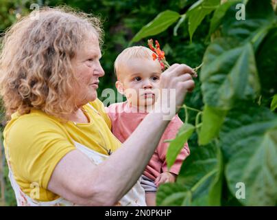 Nonna che guarda il fiore con il bambino in giardino Foto Stock