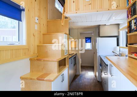 Scale in legno di pino che conducono alla camera da letto al piano superiore, alla zona cucina e alla porta del bagno sullo sfondo all'interno di una mini casa mobile di 8 x 24 metri. Foto Stock