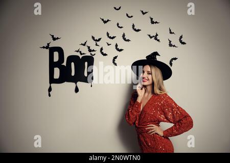 Donna in cappello di strega che posa vicino alla parete bianca decorata per Halloween Foto Stock