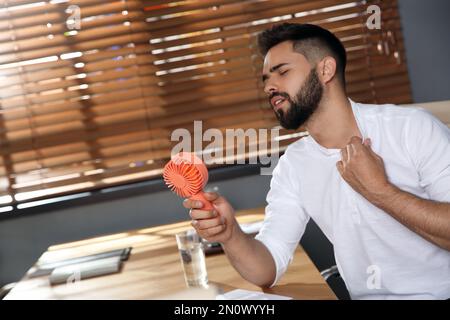 Uomo con ventola portatile che soffre di calore sul luogo di lavoro. Stagione estiva Foto Stock