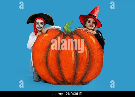 Carino bambini piccoli con zucca decorativa indossando costumi di Halloween su sfondo azzurro Foto Stock