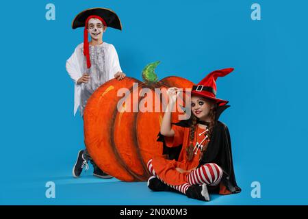 Carino bambini piccoli con zucca decorativa indossando costumi di Halloween su sfondo azzurro Foto Stock